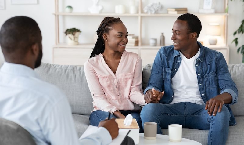 Happy Reconciled Black Spouses Holding Hands At Counselor's Office