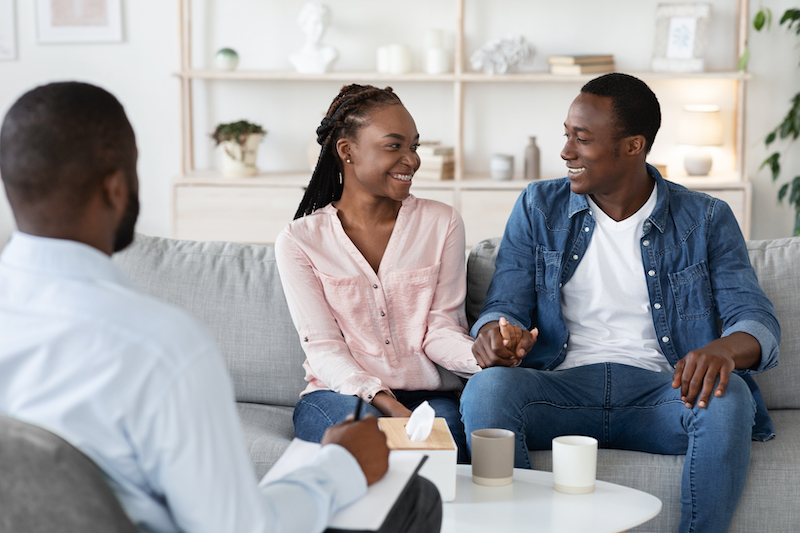 Happy Reconciled Black Spouses Holding Hands At Counselor's Office