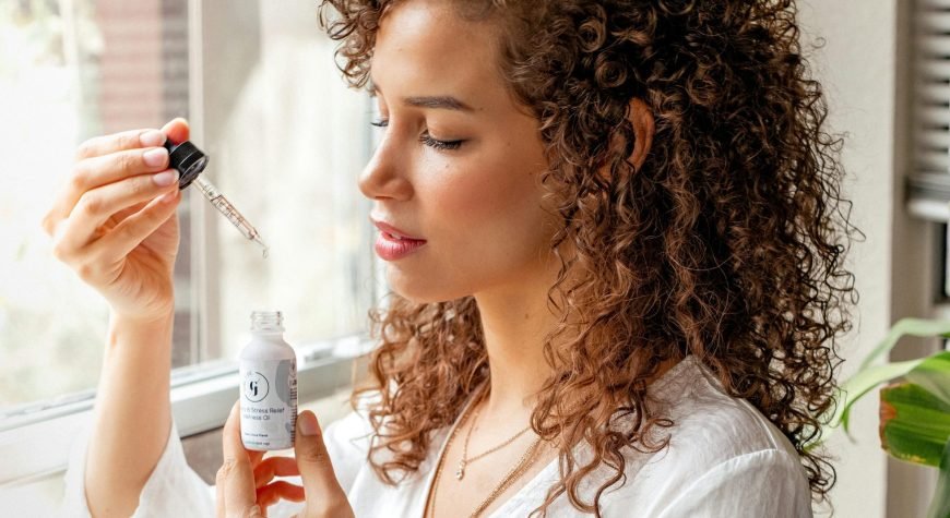 Elegant woman with curly hair applying skincare serum indoors, embracing wellness and beauty.