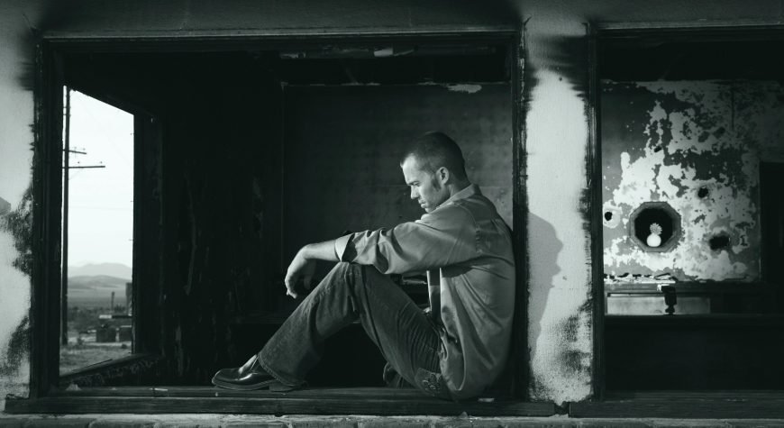 A young man sits pensively in a derelict building, embodying solitude and contemplation.